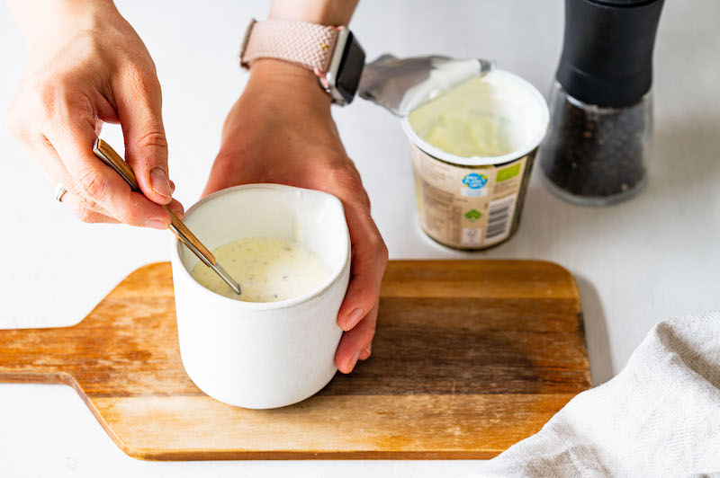 A Greek yogurt dressing is being mixed in a white jar.