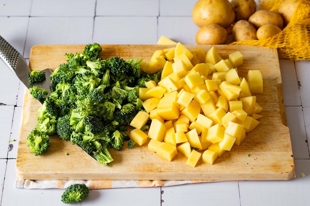Cubed potatoes and sliced broccoli on a cutting board.
