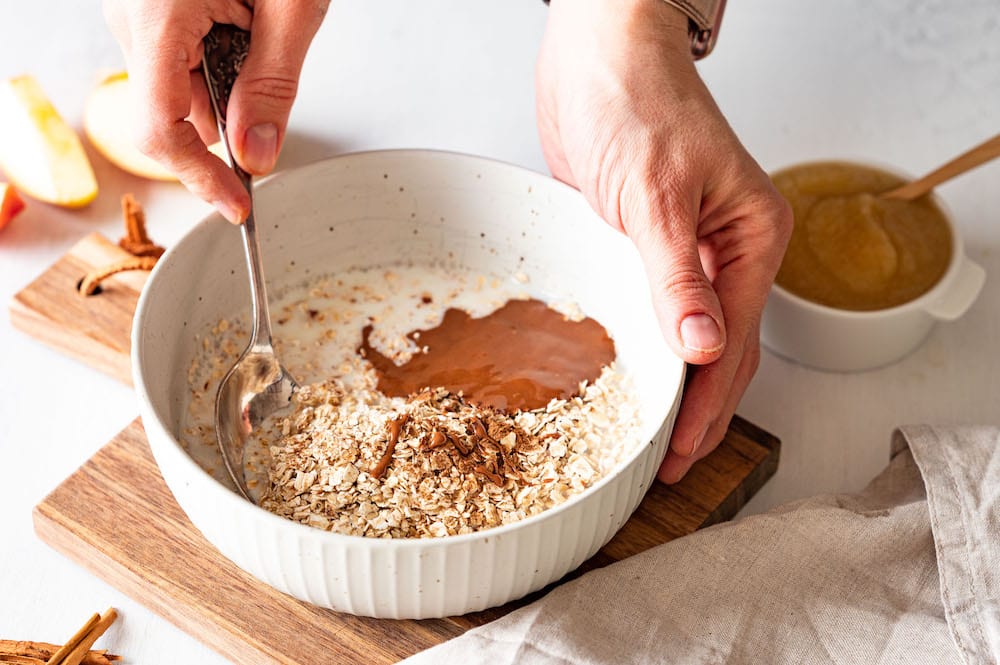 Oats, milk, almond butter and cinnamon are being combined in a bowl.