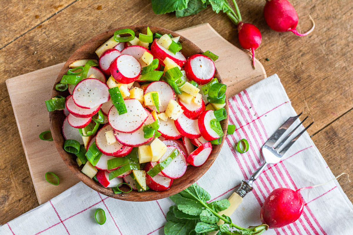 Radish salad with apples and scallions in a small wooden bowl.