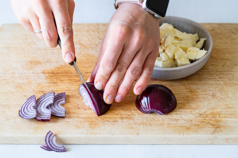A red onion is being cut into half-moon shaped. There is sliced mozzarella cheese in the background.