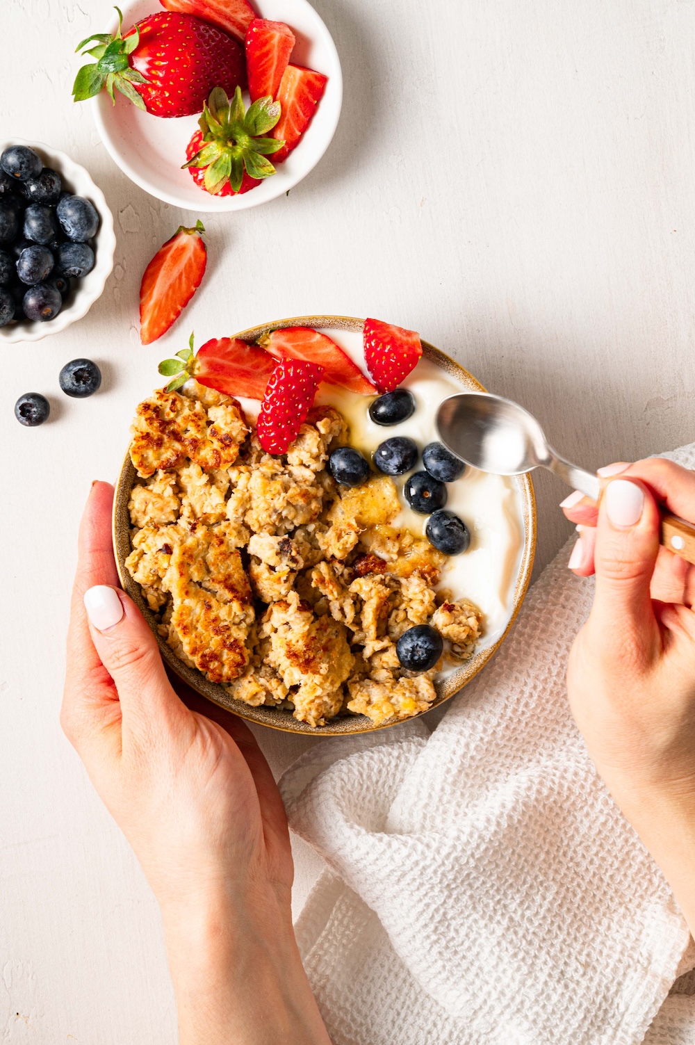 Scrambled oatmeal with yogurt and berries in a bowl, with a pair of hands and a spoon.