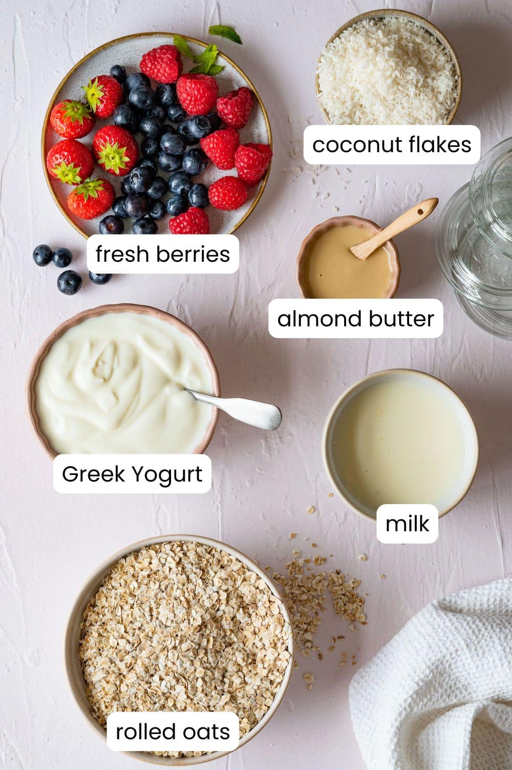 Labelled top shots of the ingredients: oats, coconut flakes, milk, greek yogurt, almond butter and fresh berries.