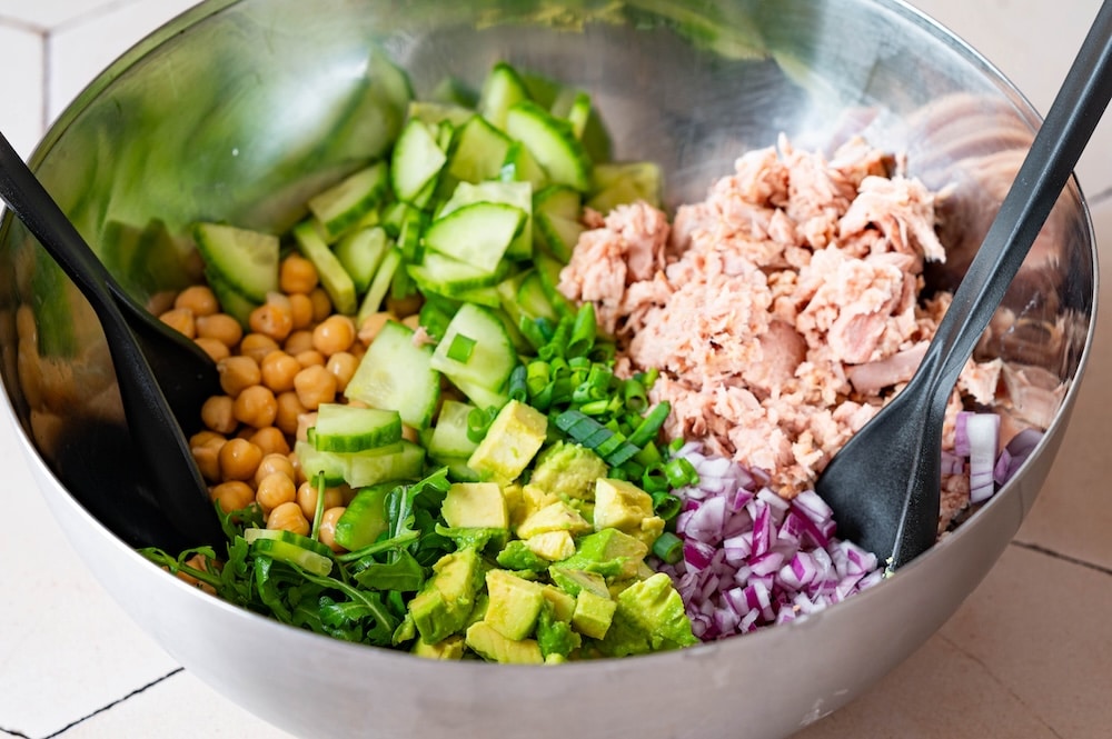 Tuna, chickpeas, avocado, arugula, red onions and scallions in a bowl.